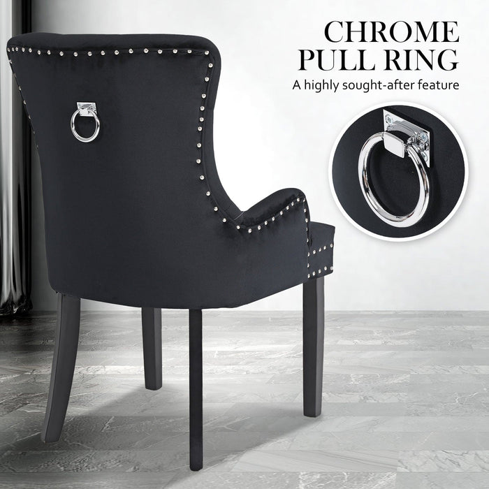 Back view of The La Bella Velvet Black French Provincial Dining Chair resting on a grey vinyl floor in front of a white wall, displaying its chrome pull ring for easy manoeuvrability 